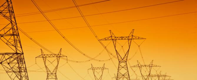 High-voltage power lines against an orange sky in a desert landscape.